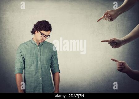 Homme stressé, cheveux bouclés porte des lunettes, regarde épuisé et déprimé, se sent honte d'être sous pression, comme plusieurs mains pointant vers le foreach Banque D'Images