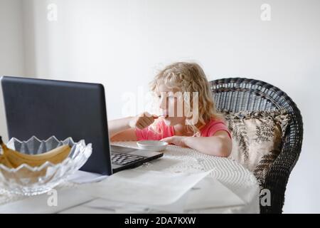 Jeune fille mangeant de la nourriture et regardant des dessins animés sur ordinateur portable. Enfant avec gadget numérique pendant le repas. Enfant utilisant des technologies modernes de divertissement tout en mangeant Banque D'Images