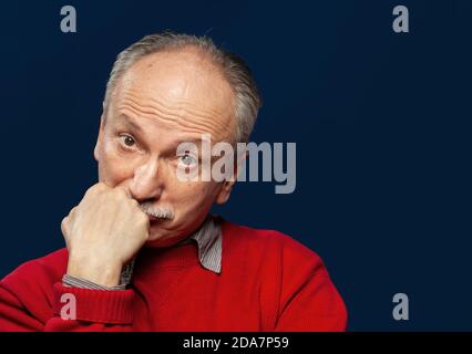 Un homme âgé sceptique props son menton avec sa main. Portrait d'un homme émotionnel âgé sur fond sombre dans le studio. Arrière-plan bleu foncé avec Banque D'Images