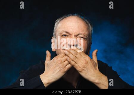 Vieux macho. Un homme âgé couvre sa bouche avec son palmsю Portrait d'un vieil homme émotionnel sur un fond sombre dans le studio Banque D'Images