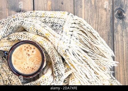 Tasse de café chaud avec mousse sur fond de table rustique en bois enveloppé d'un foulard en laine de tricot chaud. Tasse de cappuccino. Concept d'hiver, de chaleur, de vacances et d'événements. Mise au point douce. Vue de dessus. Banque D'Images