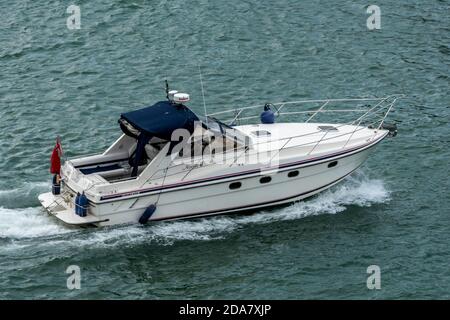 un grand bateau à moteur ou un moteur de luxe de lancement de croisière dans le solent avec cache de bimini sur la position d'helming et skipper. Banque D'Images