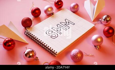 L'inscription SMM dans un carnet sur un fond rose festif. Boules de Noël rouges et roses, avions en papier autour Banque D'Images