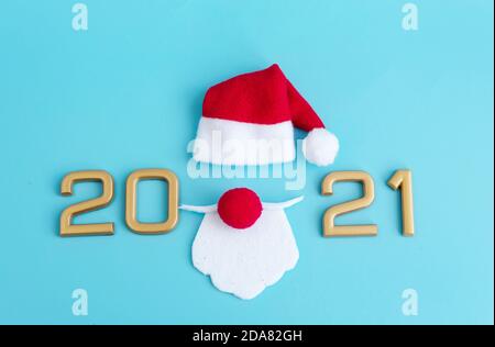 Numéros du nouvel an 2021, chapeau et barbe du Père Noël sur fond bleu, concept minimaliste créatif de Noël Banque D'Images