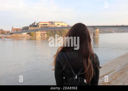 Vue arrière d'une fille avec de longs cheveux bruns, debout et regardant au loin la forteresse et le pont, édition d'automne Banque D'Images