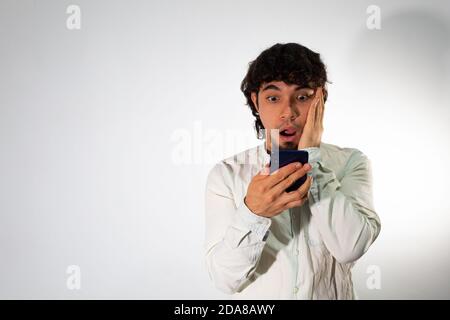 Jeune homme hispanique portant des vêtements décontractés sur fond blanc avec une expression choquée Banque D'Images