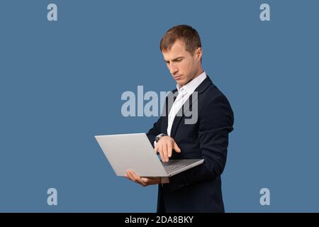 Un homme d'affaires dans un costume d'affaires regarde un ordinateur portable sur le poids dans ses mains. Studio shot concept de travail à distance sans bureau sur fond bleu Banque D'Images