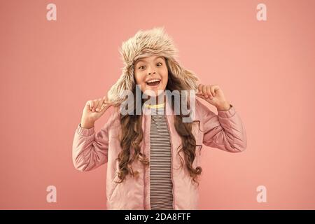 Sourire chaleureux. Bonne enfant fond rose. Vêtements chauds pour la saison froide. kid fashion trendy girl ressembler.. hipster style automne. L'activité de la petite enfance. fur hat earflap. accessoires petite fille winter hat. Banque D'Images