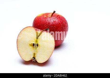 deux pommes rouges avec des éclaboussures d'eau sur un fond blanc uniforme, une pomme est coupée en moitié en regardant la tige de fruit et les graines. Banque D'Images