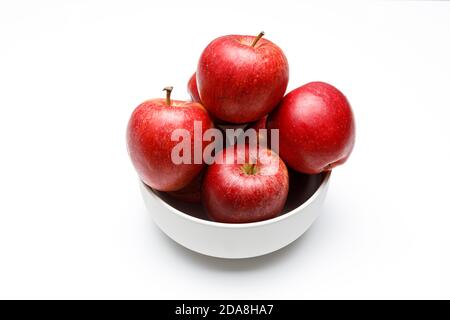 Quatre pommes rouges dans un bol en céramique blanc sur fond blanc et uniforme, vue de dessus avec ombres douces et lumière douce Banque D'Images