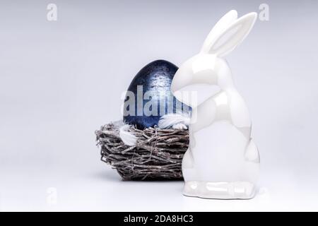 Lapin blanc de pâques figure sur fond blanc uniforme avec un nid de pâques fait de branches brunes en arrière-plan, bleu royal oeuf de pâques, idées de décoration Banque D'Images