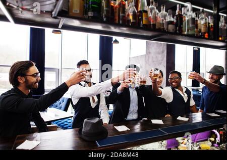 Santé ! Groupe de gangsters d'homme élégants et rétro bien habillés passent du temps au club. Boire du whisky au comptoir du bar. Parti multiethnique masculin Bachelor mafia Banque D'Images