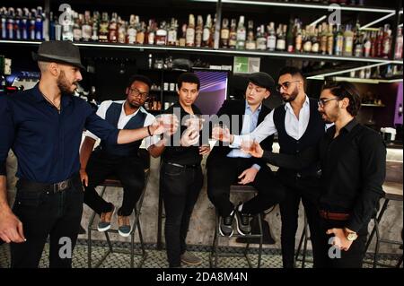 Santé ! Groupe de gangsters d'homme élégants et rétro bien habillés passent du temps au club. Boire du whisky au comptoir du bar. Parti multiethnique masculin Bachelor mafia Banque D'Images