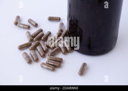 Bouteille en plastique ambré avec bouchon brun ouvert et debout, avec quelques pilules d'un médicament ou d'un supplément alimentaire tombé sur une surface blanche Banque D'Images