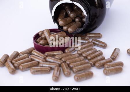 Bouteille en plastique ambré avec couvercle brun est tombé ouvert, avec de nombreuses pilules d'un médicament ou d'un supplément alimentaire qui se déverse de la bouteille sur une surface blanche Banque D'Images