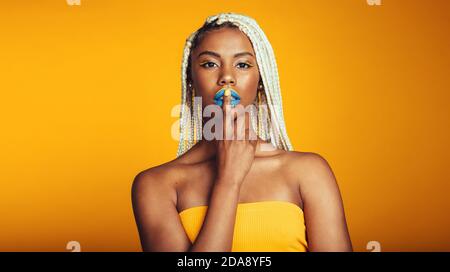 Gros plan de la femme avec des lèvres peintes sur fond jaune. Portrait d'une femme afro-américaine artistique avec des cheveux tressés montrant shh. Banque D'Images