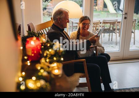 Couple senior utilisant une tablette pour les appels vidéo de leur famille le soir de Noël. Homme et femme senior regardant la tablette numérique et souriant pendant Banque D'Images