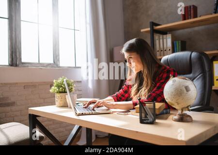 Le télétravailleur fille travaille à la maison avec un ordinateur portable. Elle travaille intelligemment en raison de la pandémie de Covid-19 Banque D'Images