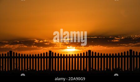 Coucher de soleil et une clôture de piquetage. Photo générique du coucher de soleil à travers une clôture de piquetage. Banque D'Images