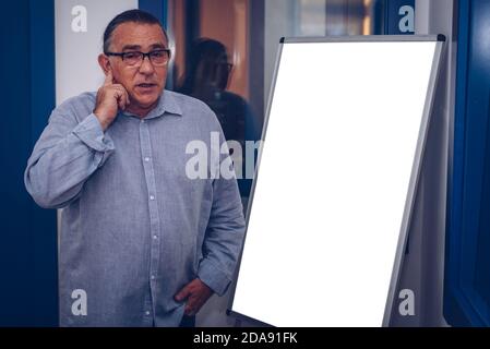 un homme adulte avec des lunettes et fait une présentation de des idées devant un tableau noir touchant son visage Banque D'Images