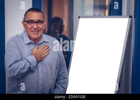 un homme adulte avec des lunettes et fait une présentation de idées devant un tableau noir touchant sa poitrine Banque D'Images