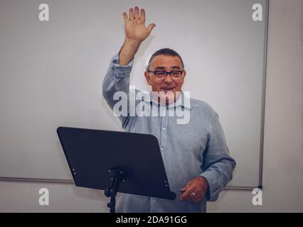 un homme adulte avec des lunettes fait une présentation à un lutrin et en levant la main Banque D'Images