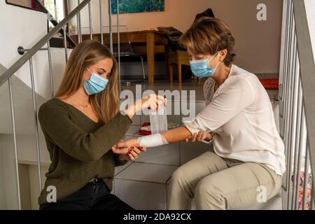 Premiers soins dans des conditions de corona, application d'un bandage, après un accident à la maison, avec un masque de nez et de bouche, lors de l'octroi de premiers soins Banque D'Images