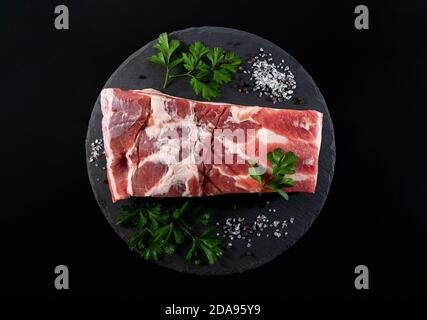 Poitrine de porc, poivre noir, sel de roche et persil italien sur un plateau en pierre noire UNE vue d'en haut Banque D'Images
