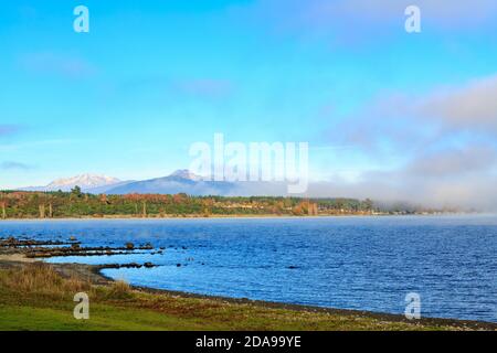 Lac Taupo, Nouvelle-Zélande, avec brume matinale qui s'élève de l'eau. À l'horizon se trouvent les montagnes du parc national de Tongariro Banque D'Images