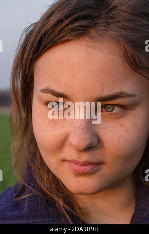 Visage de fille avec des taches de rousseur sur fond vert et lumière du soleil du soir. Banque D'Images