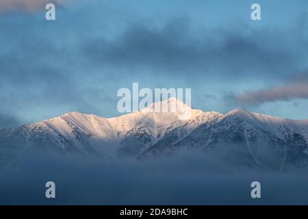 Le soleil se lève sur la pente est enneigée de Saddle Mountain, dans la chaîne de Lemhi, entourée de nuages le matin d'hiver.