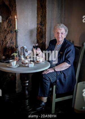 Femme de 90 ans, non agénaire anglaise célébrant son anniversaire avec un verre de vin rouge dans un restaurant aux chandelles. Angleterre Royaume-Uni Banque D'Images