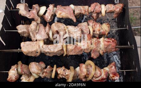 Tranches de viande avec des rondelles d'oignon placées sur une brochette, le kebab lentement rôti dans la fumée du gril. Loisirs en plein air. Banque D'Images