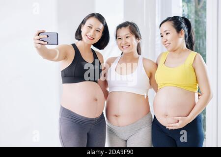 Jolie femme enceinte asiatique souriante prenant selfie avec d'autres enceintes les femmes après les cours de yoga Banque D'Images