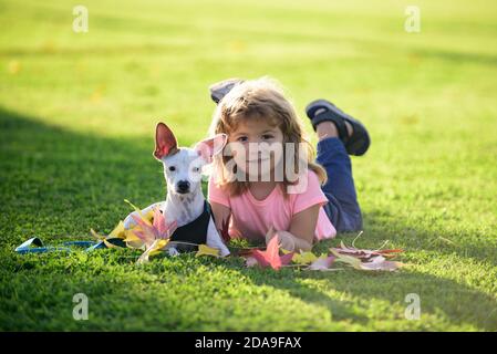 Drôle d'enfant avec chien de chiot. Adolescent dans le parc jouer avec un chien. Blonde heureux garçon avec son chien chihuahua couché sur pelouse. Banque D'Images