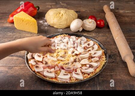 femme qui fait de la pizza maison. Préparation de la pizza, gros plan de la pizza à la main avec du fromage sur une table rustique en bois sombre Banque D'Images