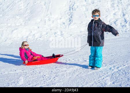 Frère tirant sa sœur enfants luge neige de traîneau. Petite fille et petit garçon en traîneau. Enfants traîneaux. Les enfants jouent à l'extérieur dans la neige. Traîneau pour enfants. Banque D'Images