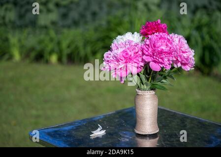 Bouquet de fleurs de pivoines roses et blanches dans un vase sur une table en plein air en été. Banque D'Images