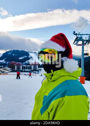 Homme heureux en tenue de ski avec le père Noël Noël rouge hat au winter mountains hill Banque D'Images