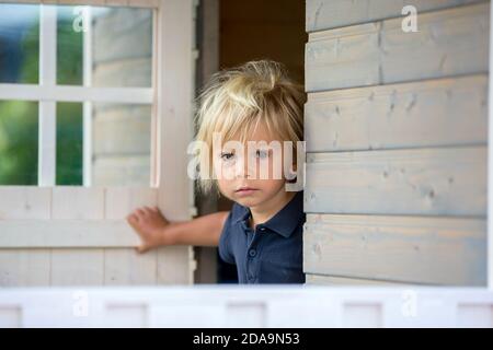 Adorable petit garçon, jouant dans une maison de poupée en bois dans le jardin, regardant dehors Banque D'Images