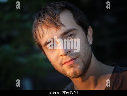 Portrait de mise au point douce d'un jeune homme dans les rayons du soleil couchant. Concentrez-vous sur les yeux. DOF peu profond Banque D'Images