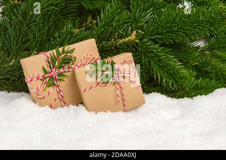 Deux cadeaux de Noël faits main sans plastique sous un sapin. Cadeaux enveloppés dans du papier artisanal et un support à nœud en corde dans la neige avec des branches de pin comme arrière-plan Banque D'Images