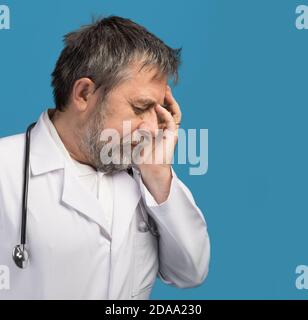 Portrait d'un médecin fatigué avec la main près de sa tête, regardant totalement stressé. Isolé sur fond bleu avec espace de copie Banque D'Images