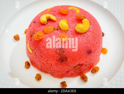 Magnifique monticule de Kesari rose prêt à manger dans une assiette blanche garnie de noix de cajou et de raisins secs Banque D'Images