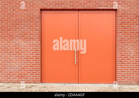 Double porte fermée pivotante métallique orange industrielle dans un mur en brique rouge. Remplacement de l'arrière-plan Banque D'Images