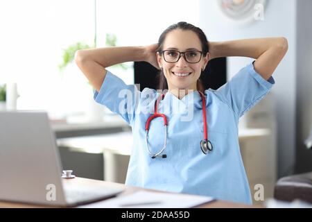 Jeune médecin souriant assis à table par ordinateur portable et tenant rendez-vous en clinique Banque D'Images