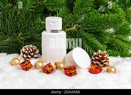 Ensemble de produits cosmétiques de soin de la peau d'hiver dans la neige sous l'arbre de Noël avec des cadeaux, des cônes de pin et des boules. Pot de crème pour le visage et flacon de lotion pour le corps Banque D'Images