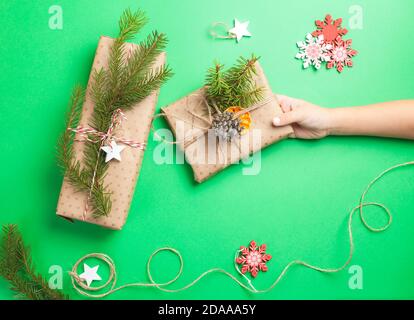 Zéro déchet Noël cadeaux boîtes emballées dans papier artisanal sur fond vert . La main d'enfant peut contenir un cadeau Banque D'Images