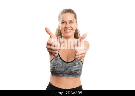 Femme adulte souriant faisant le double pouce-up comme un geste dans la salle de gym entraînement sportswear comme d'accord avec le concept sportif sain de style de vie isolé sur blanc Banque D'Images