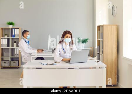 Médecins en visage couvrant des masques travaillant sur des ordinateurs assis à bureaux dans le bureau de l'hôpital Banque D'Images